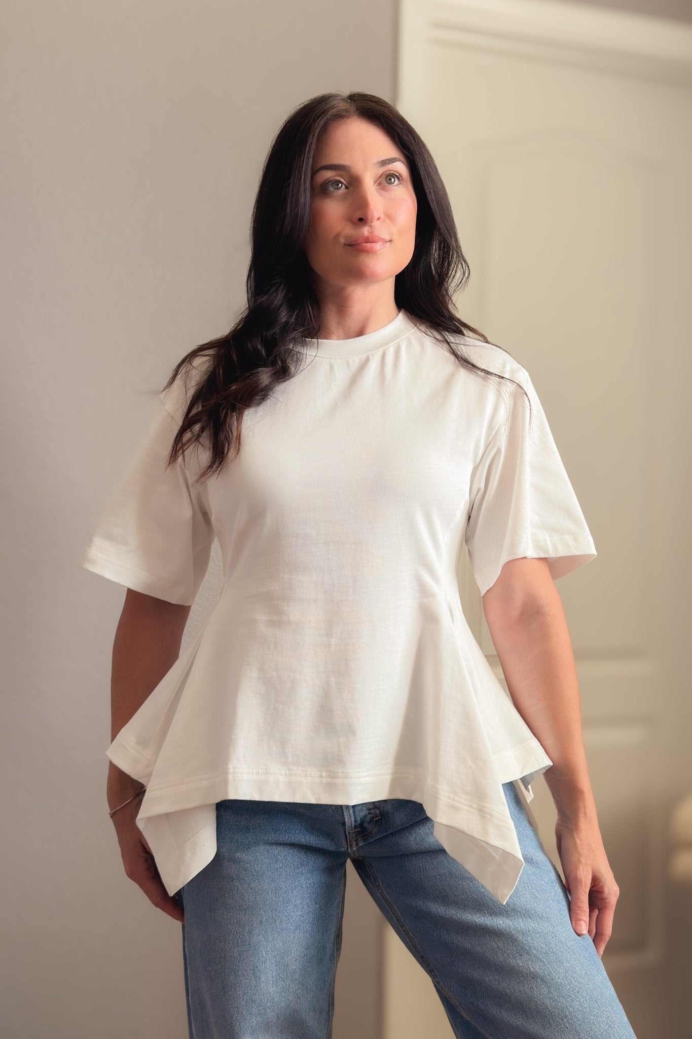 White structured cotton peplum T-shirt photographed indoors, showing the oversized sleeves and flattering waist-defining shape.