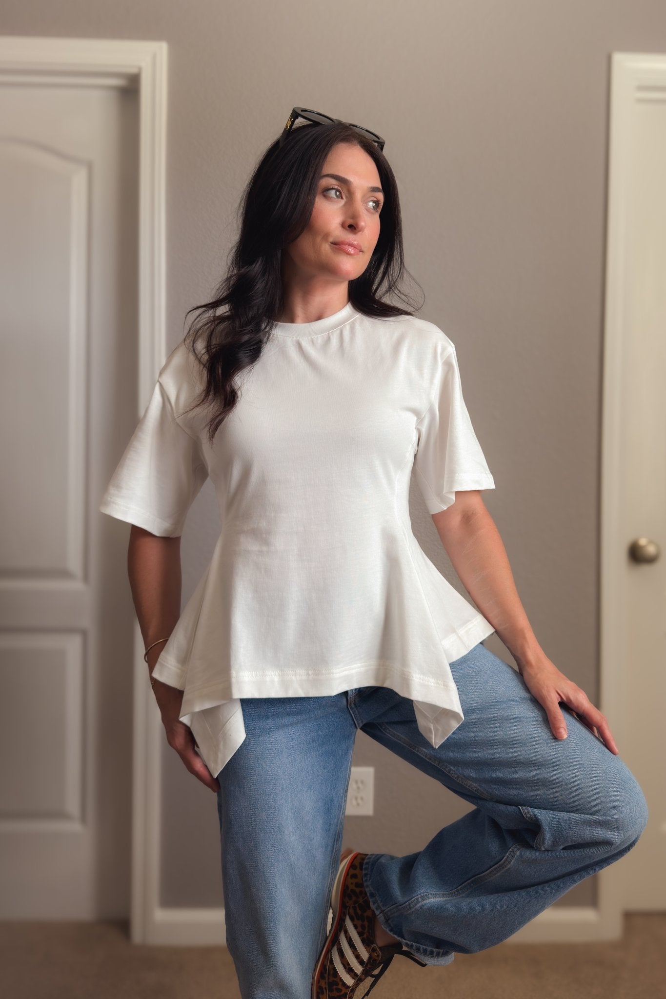 White structured cotton peplum T-shirt photographed indoors, showing the oversized sleeves and flattering waist-defining shape.