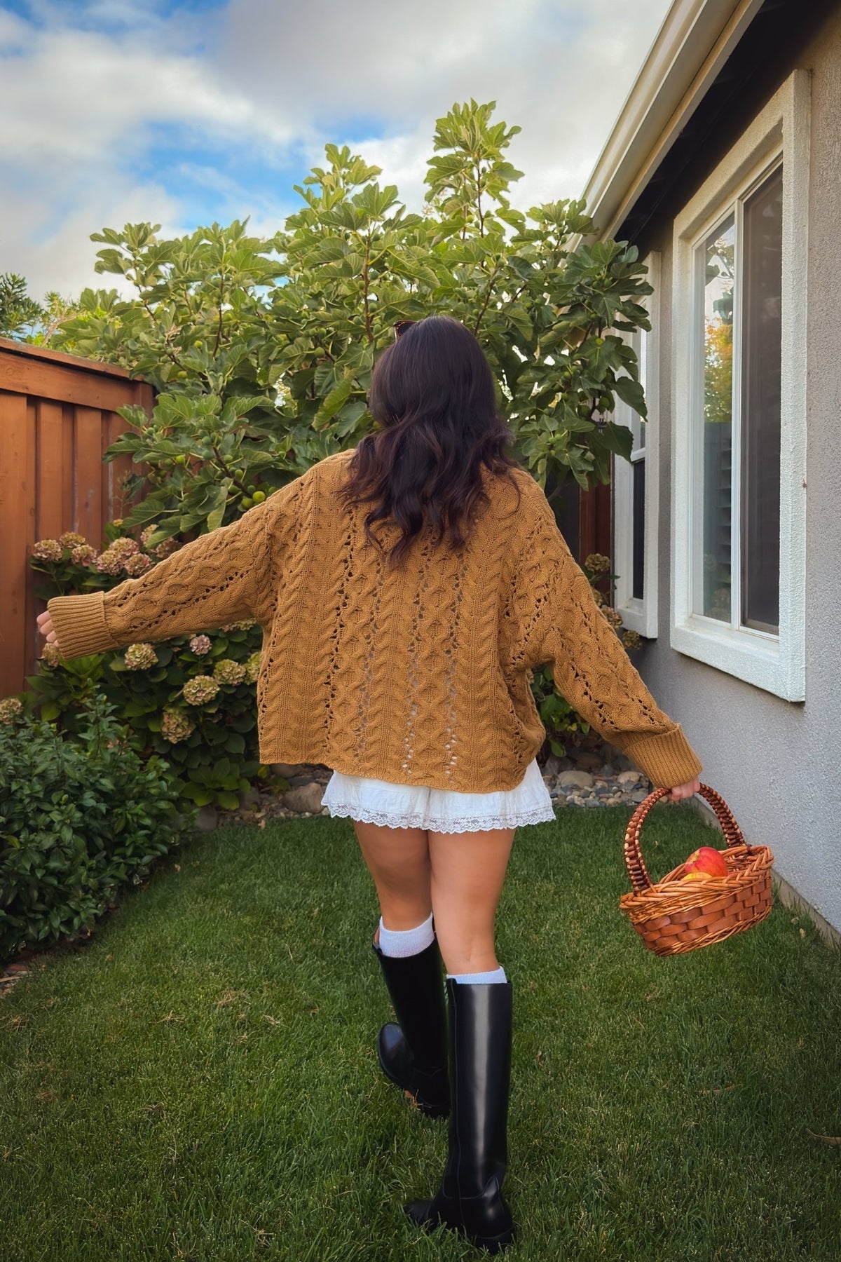 Women’s camel sweater styled with white shorts and black knee high boots