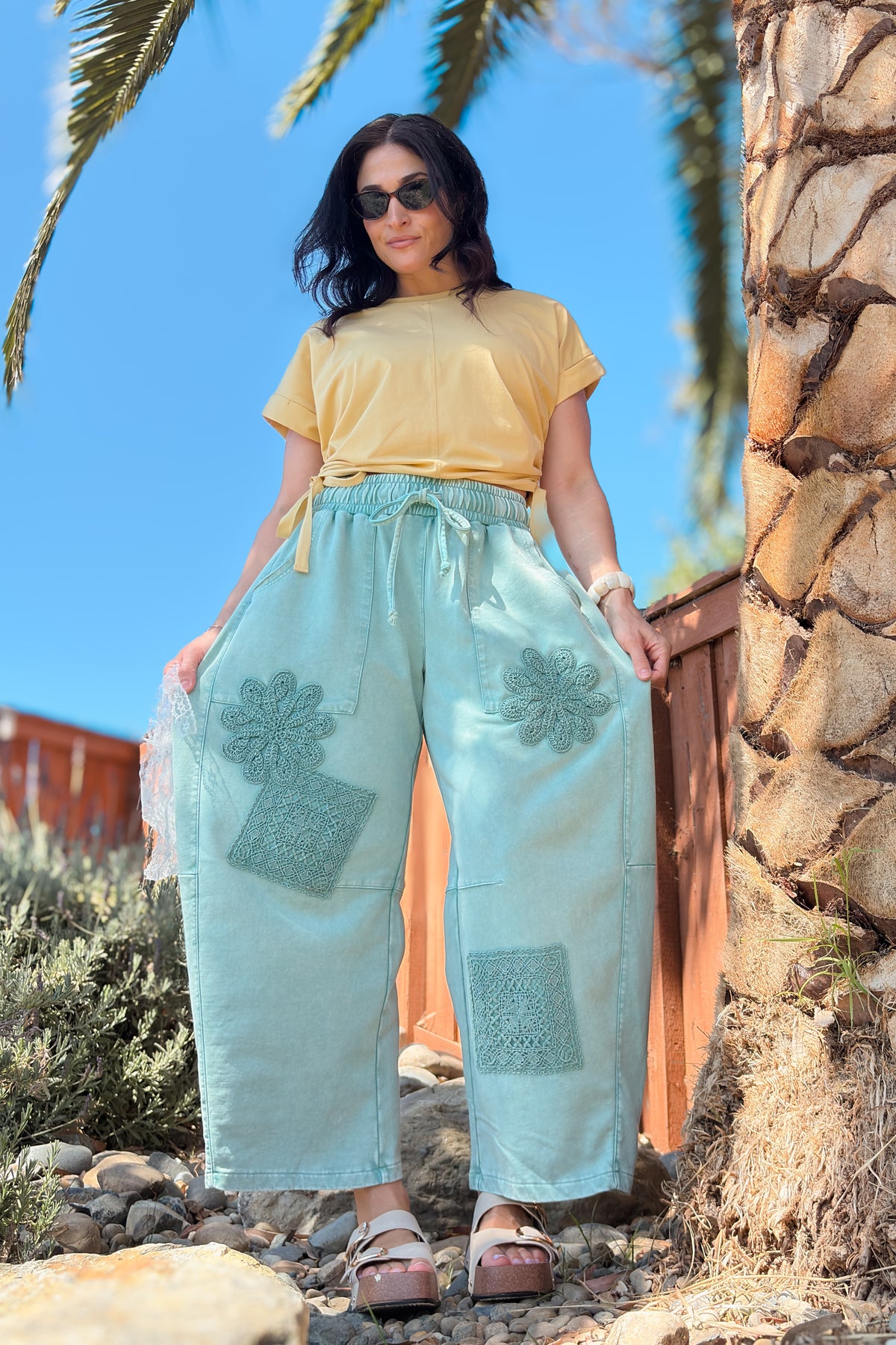 Close-up of floral crochet appliqué detailing on green mineral wash French terry barrel pants.