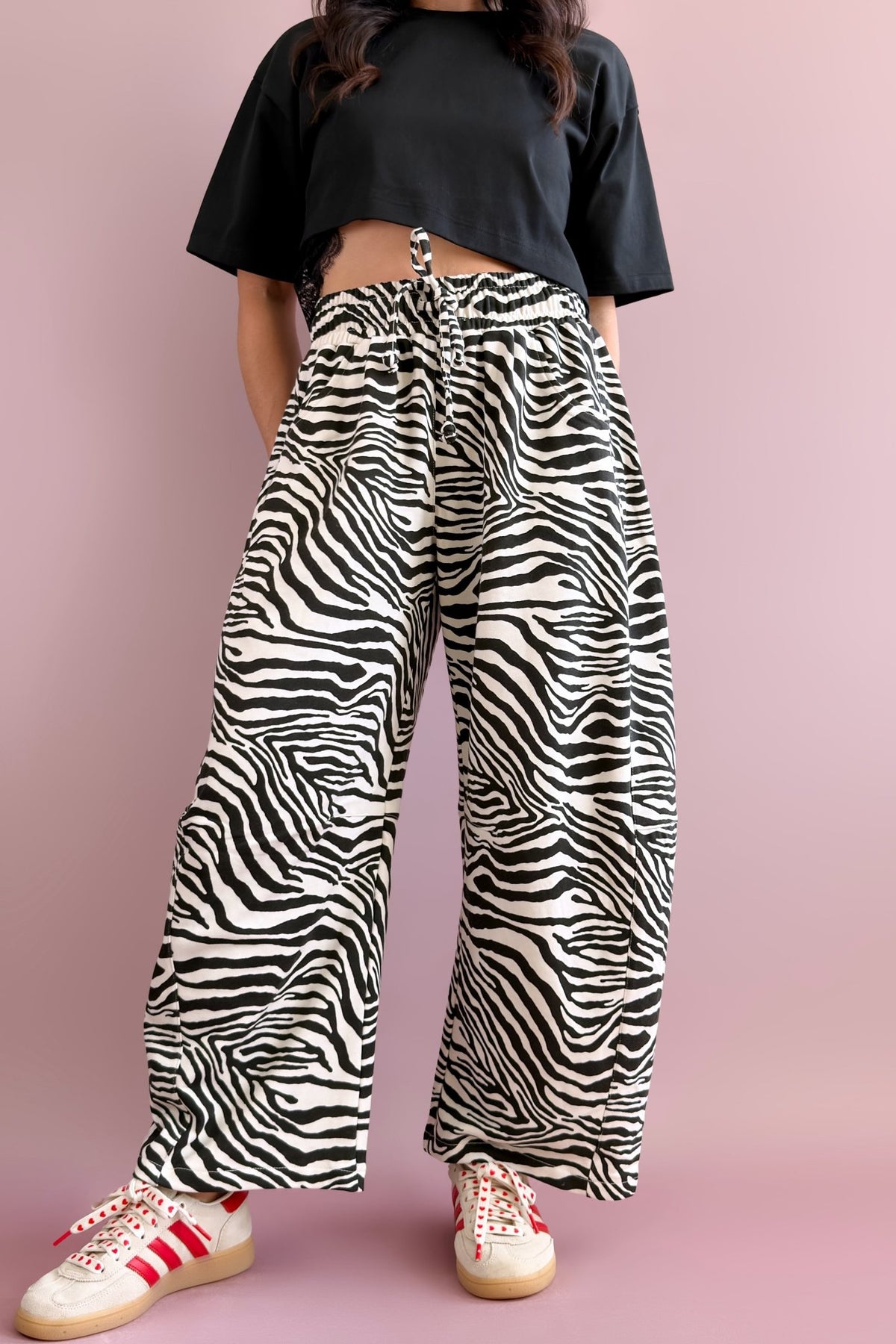 Woman wearing black and ivory zebra print French terry barrel pants with a black cropped tee and white sneakers with red stripes