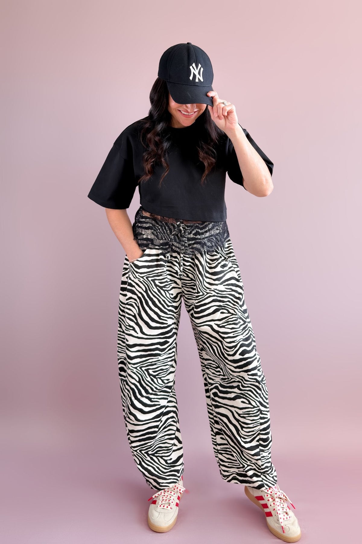 Casual outfit with black and ivory zebra print barrel pants, black cropped tee, baseball cap, and sneakers