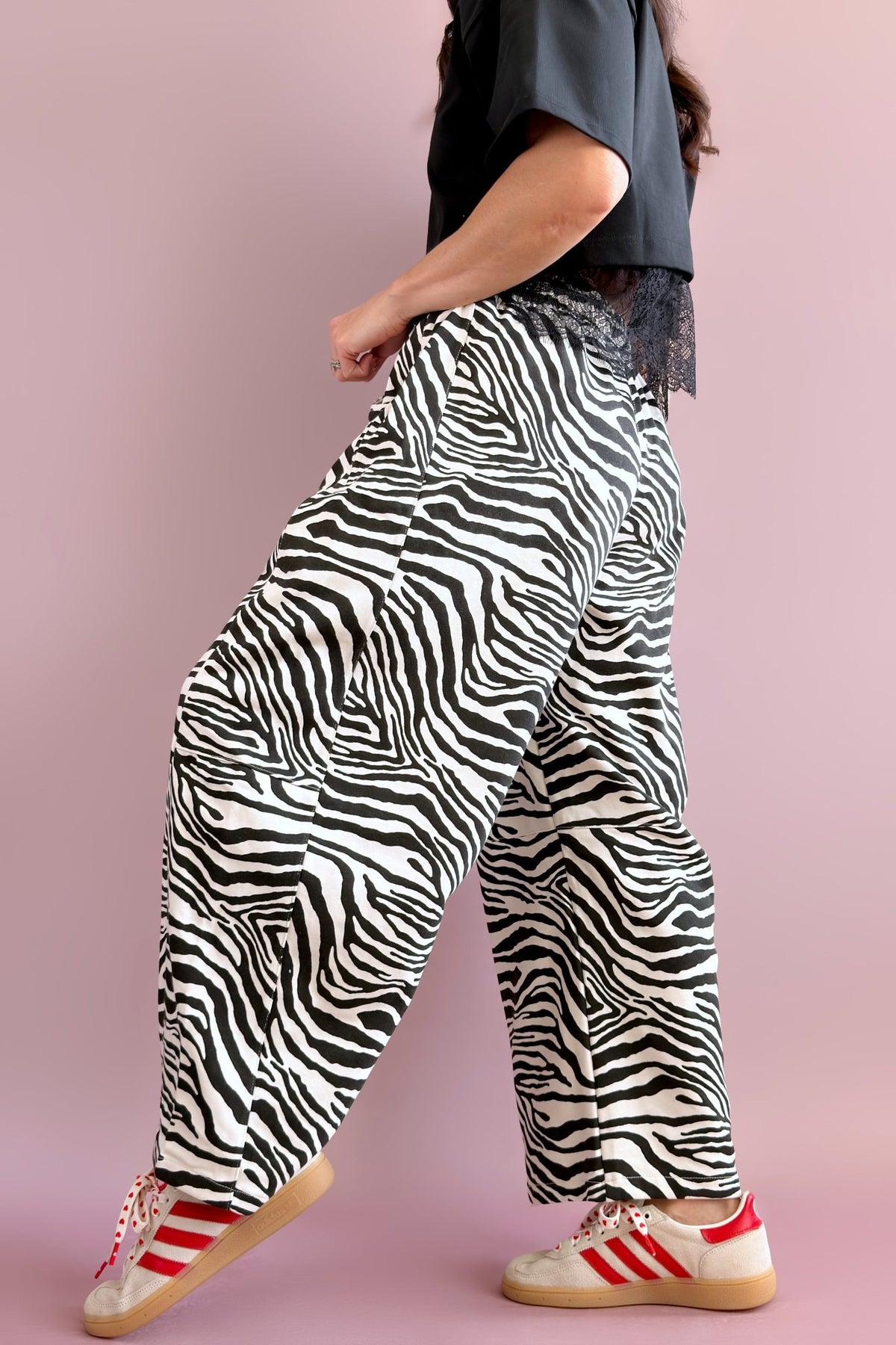Full-length outfit featuring black and ivory zebra barrel pants styled with a black cropped top, baseball cap, and sneakers